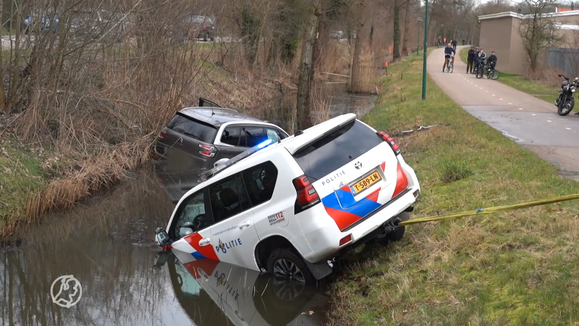 Politieauto wil inzittenden auto in sloot redden, vergeet handrem en rijdt zelf sloot in