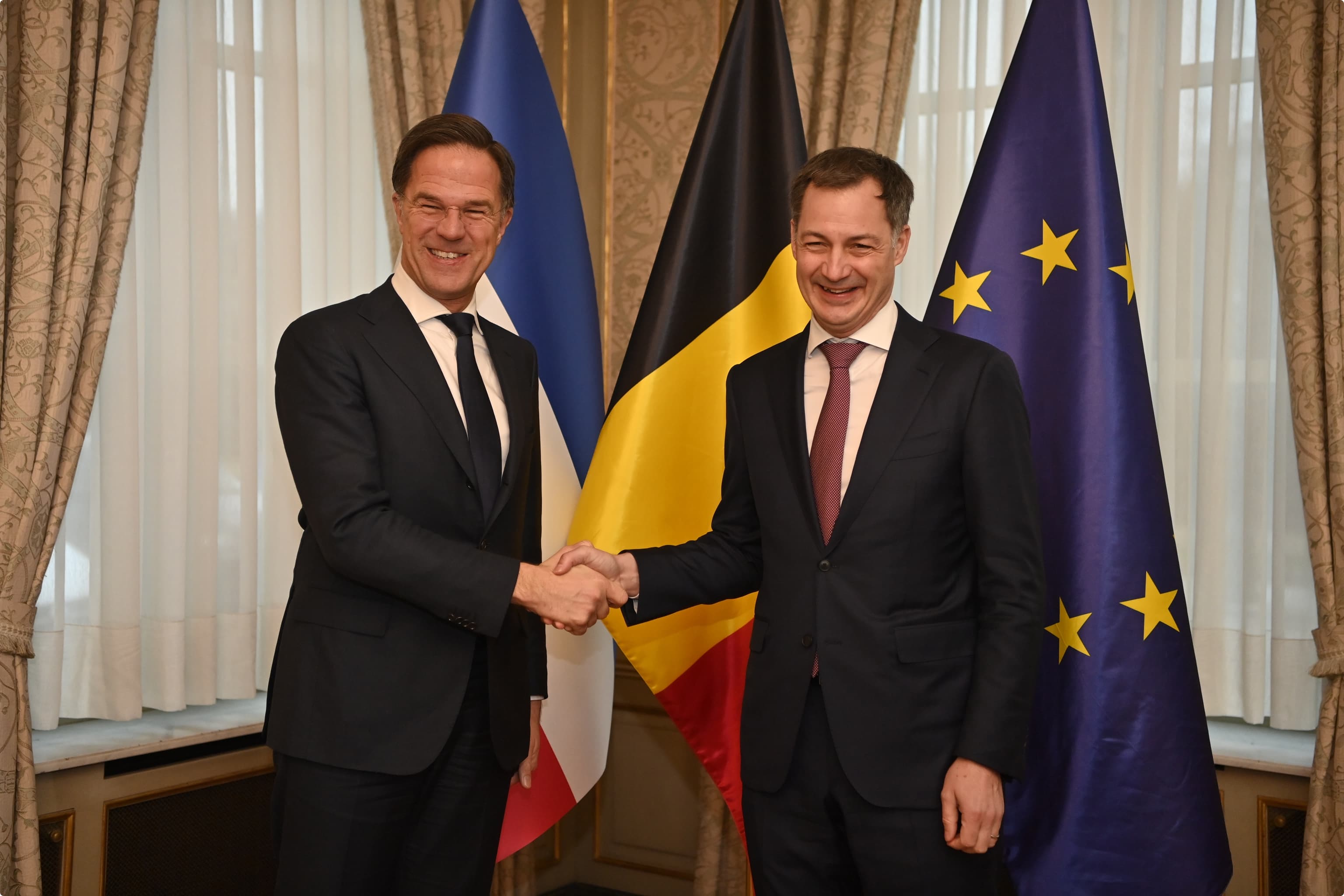 Rutte en De Croo geven elkaar een hand voor een aantal vlaggen. De Nederlandse vlag hangt omgekeerd.