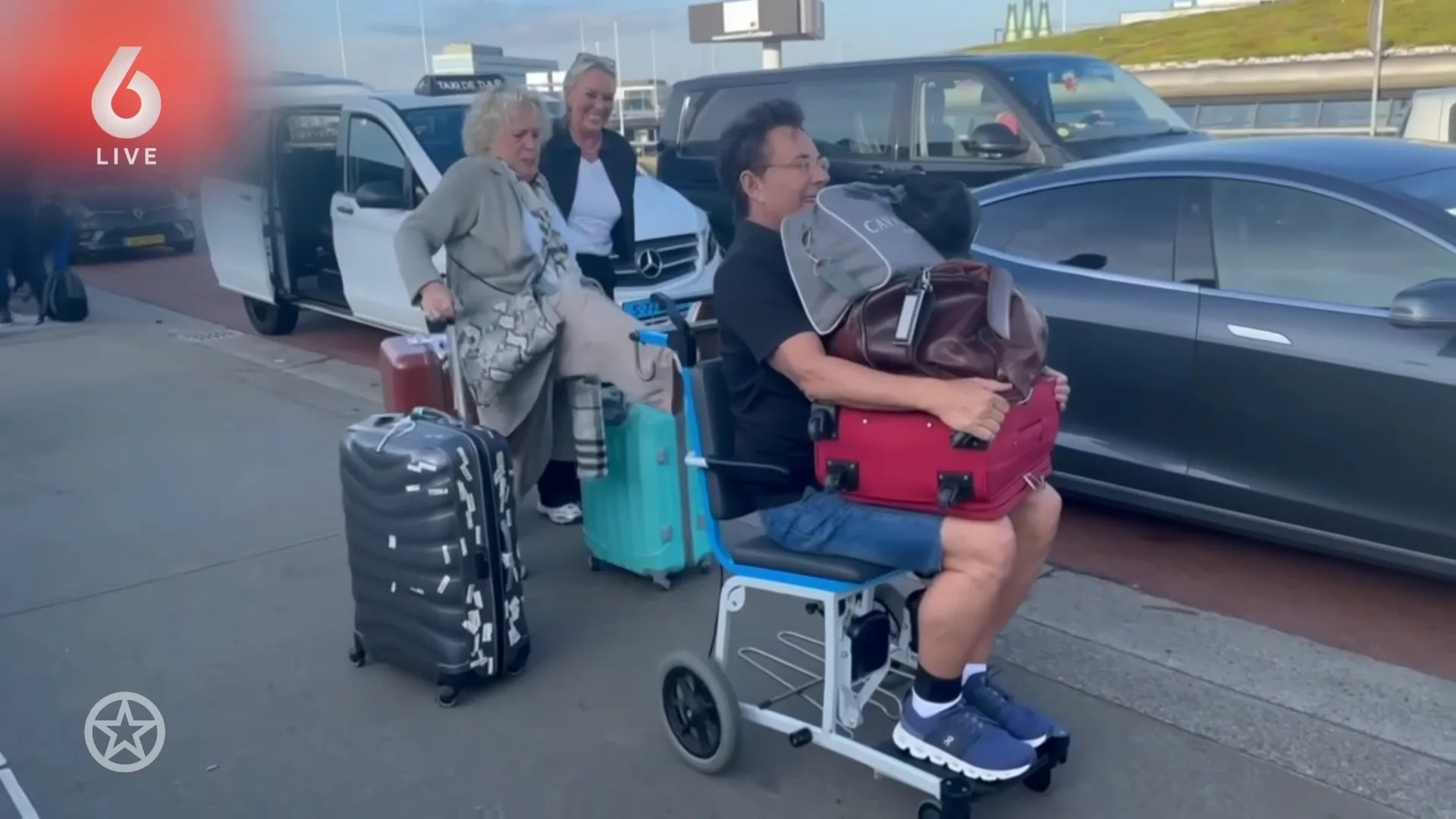 Gerard Joling in een rolstoel door Schiphol