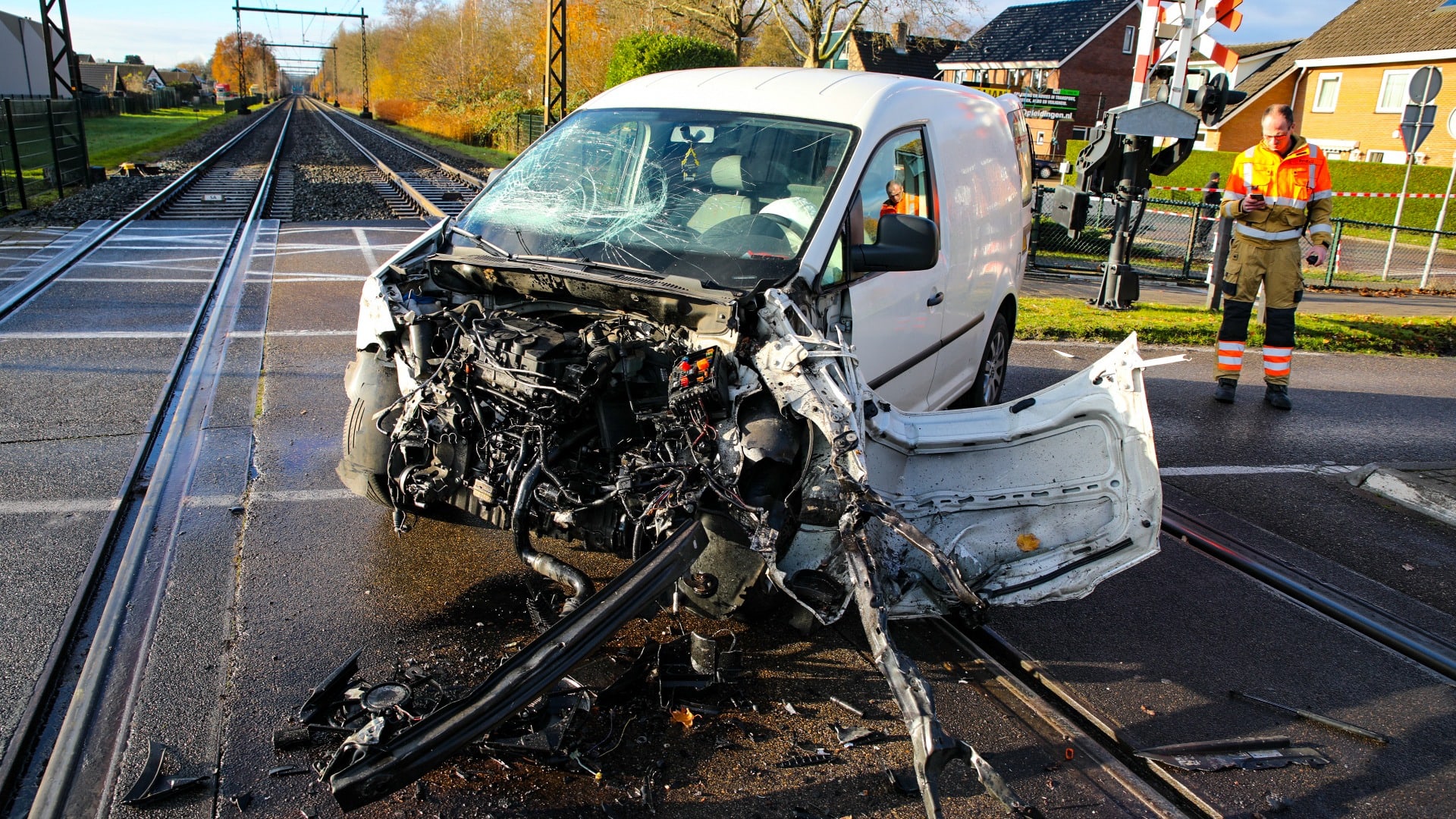 Bestelbus uiteengereten door botsing met trein, bestuurder stapt levend uit