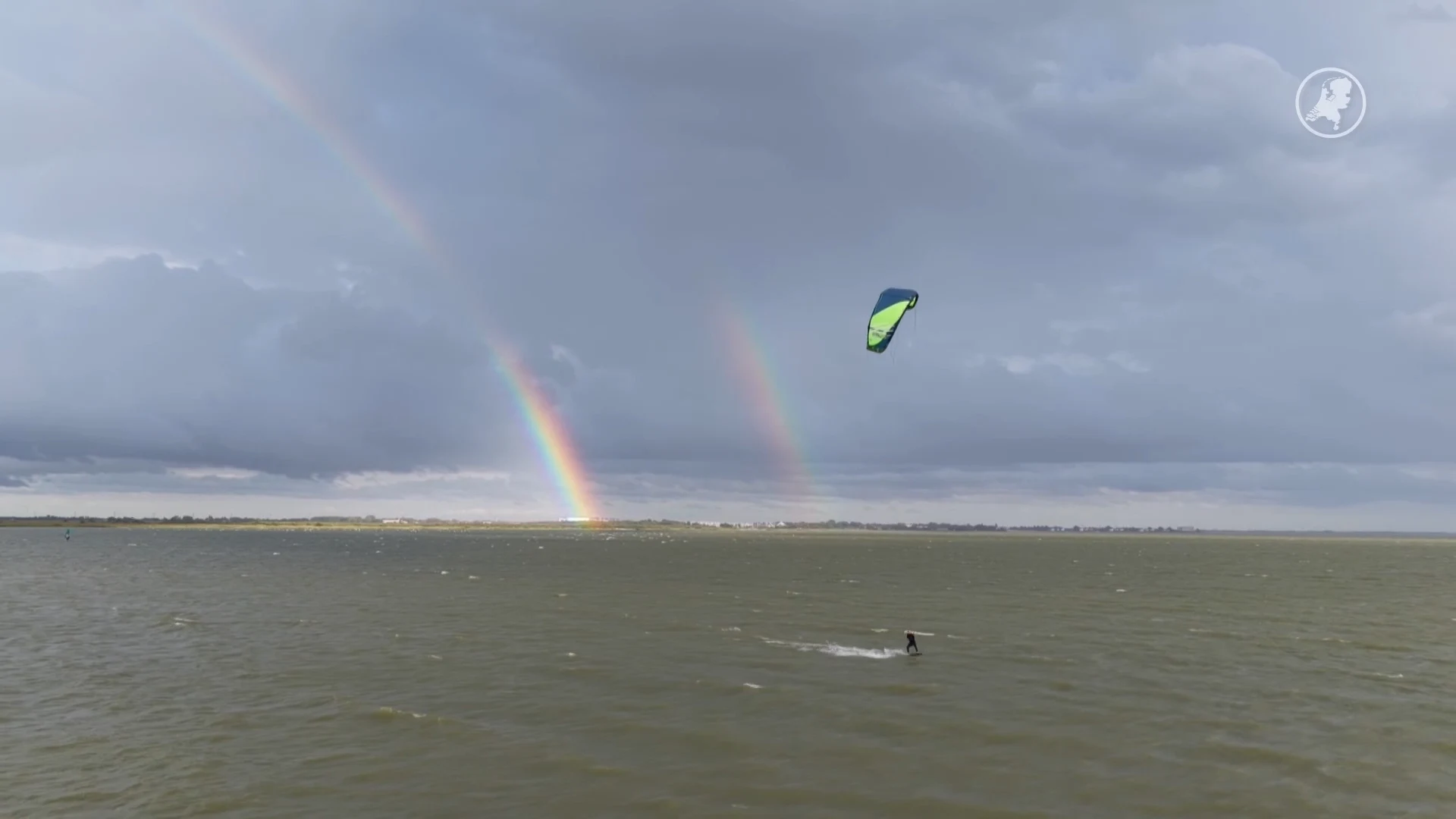 Prachtige beelden van surfers op het water tijdens dubbele regenboog